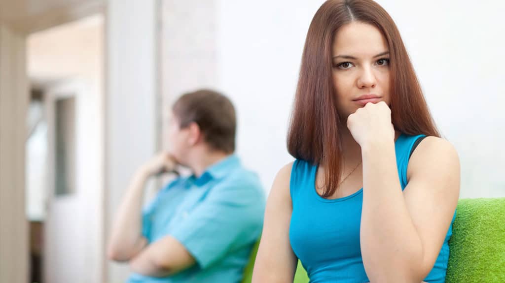 Upset young couple sitting on a couch turned away from each other, with woman in the foreground