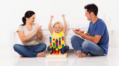 Mom and dad sitting on the floor with their young daughter and applauding her as she cheers over building tall block towers
