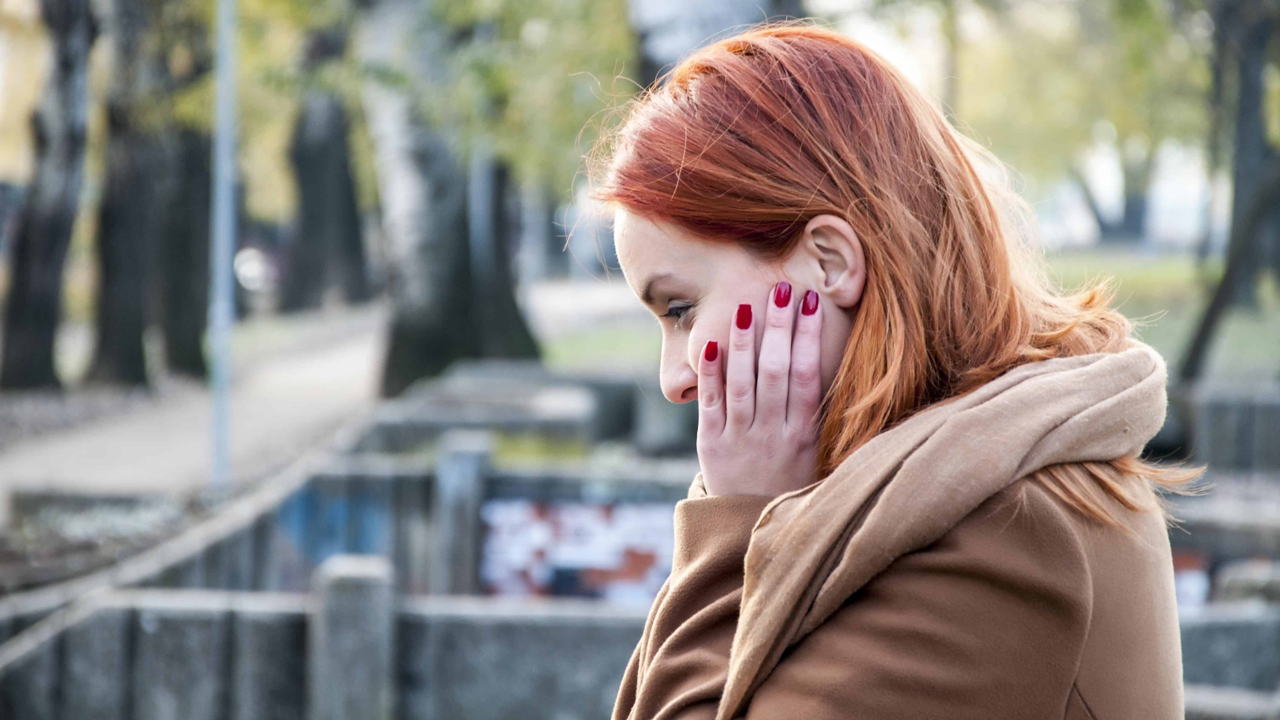 Profile of woman standing outside looking down pensively