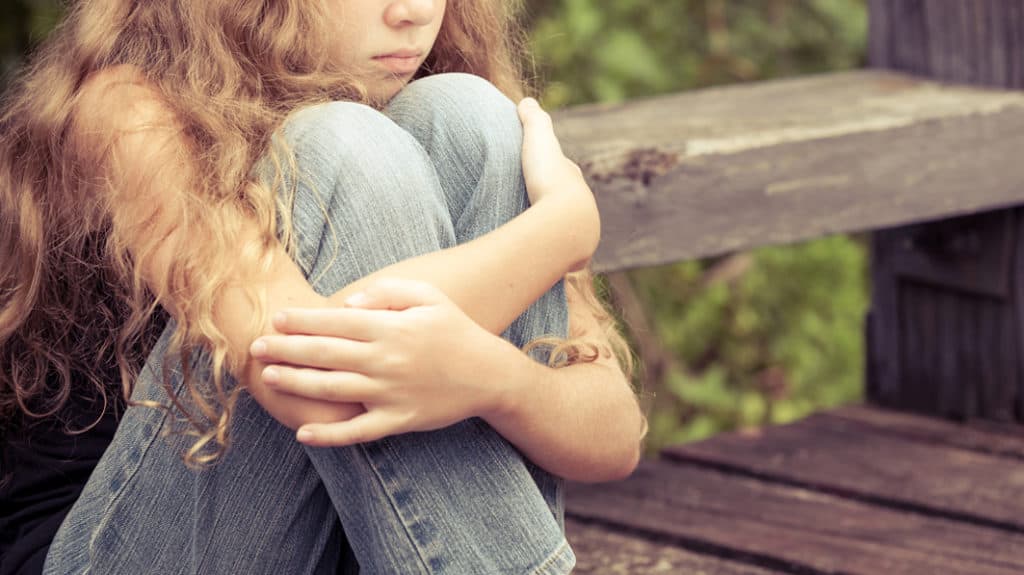 Young sad girl sitting and hugging her knees to her chest