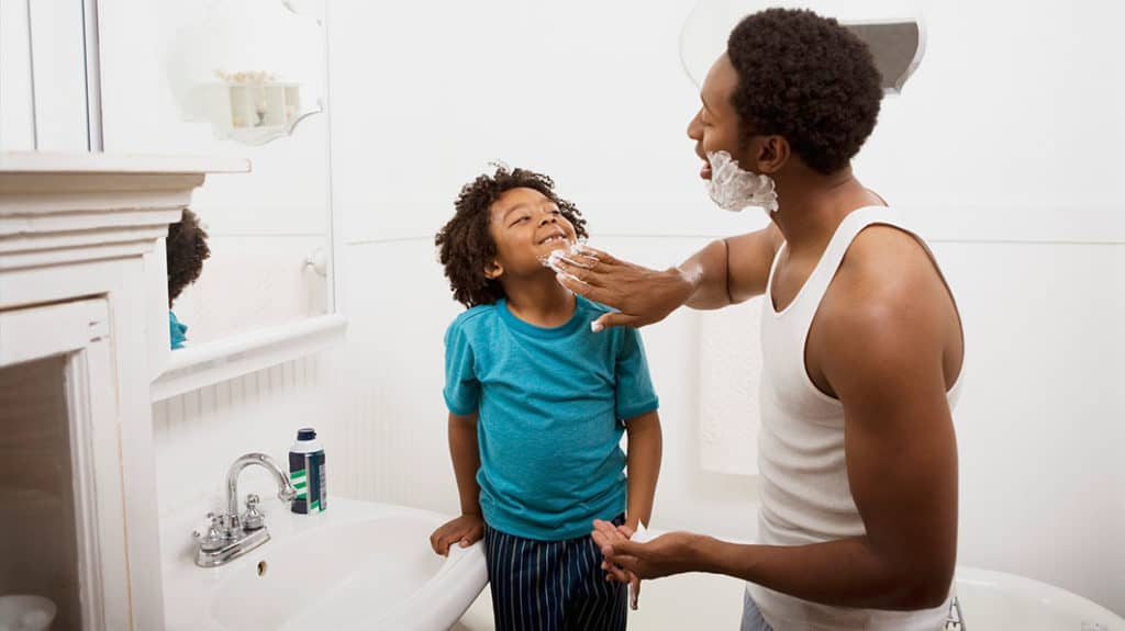 Dad applying shaving cream to his young son's face to teach him how to shave