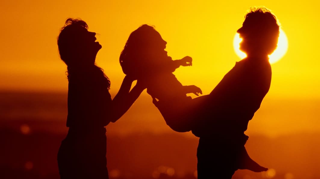 Silhouette of laughing family at sunset with dad holding young daughter