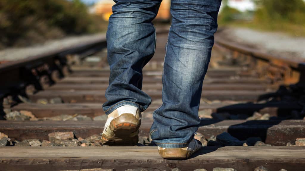 Closeup of the lower back side of a man's legs walking down railroad tracks