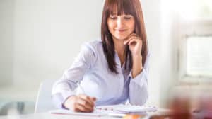 Young, smiling businesswoman sitting at a desk and writing in a notebook