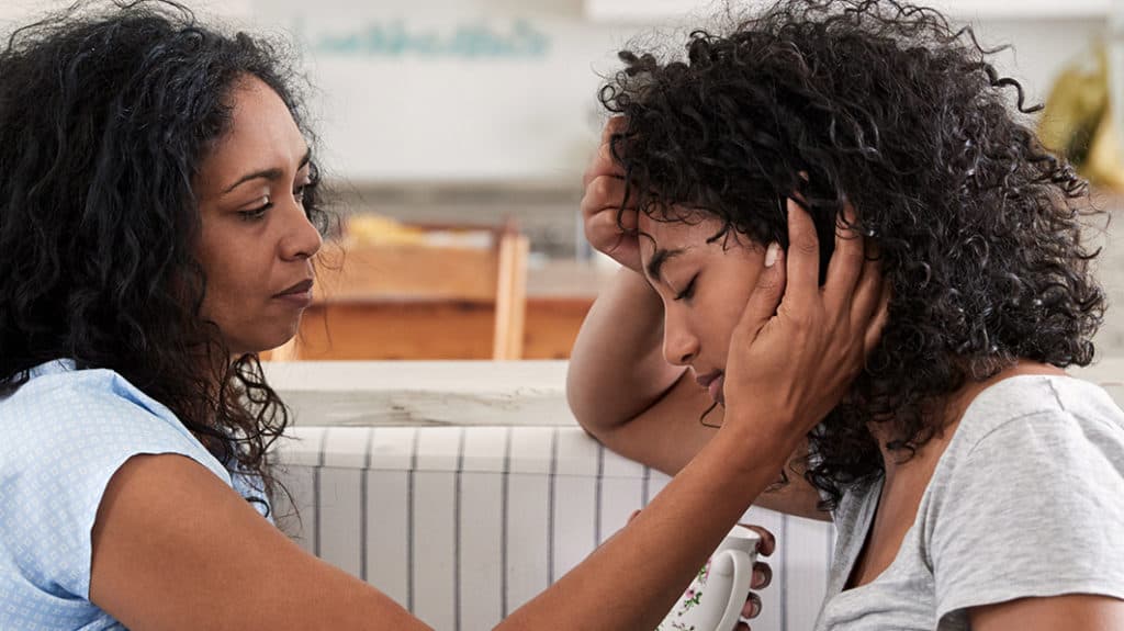 African-American mom comforting her troubled teen daughter