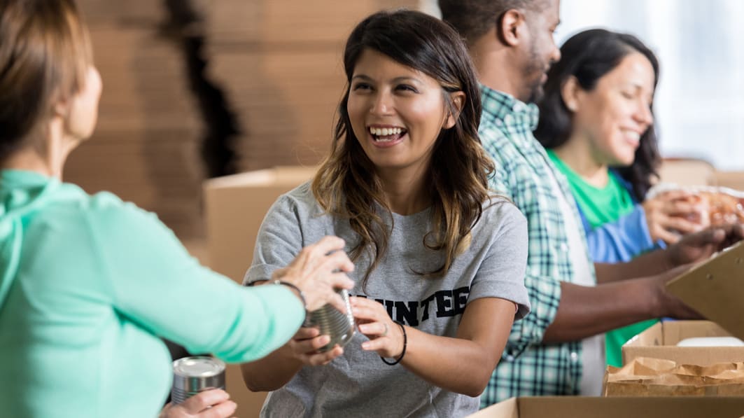 Young, smiling woman working as a volunteer in a food line and being handed canned goods