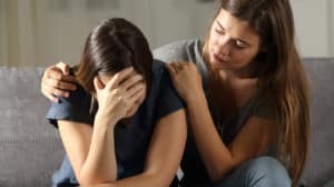 Teen girl comforting her crying friend while seated on a couch