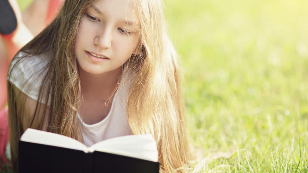 Teen girl lying on the grass and reading a book