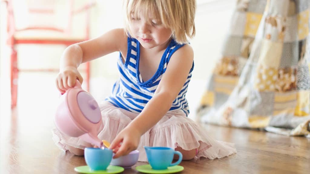 Little girl sitting on the floor and playing with a toy tea cup set