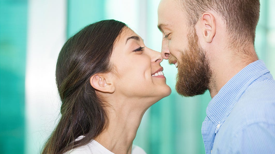 Close up of young, smiling couple with their noses touching, like they're about to kiss