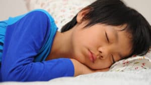 Close up of young Asian boy's face as he's lying on a pillow sleeping peacefully with his head resting on his hand.