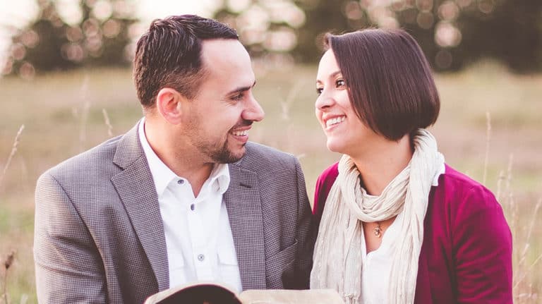 Nicely-dressed, smiling couple looking at each other while sitting in a grassy field.