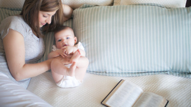 Mother lying on bed with her baby with an open Bible off to the side.