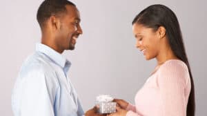 Close-up profile image of a smiling man handing a small wrapped present to a smiling woman