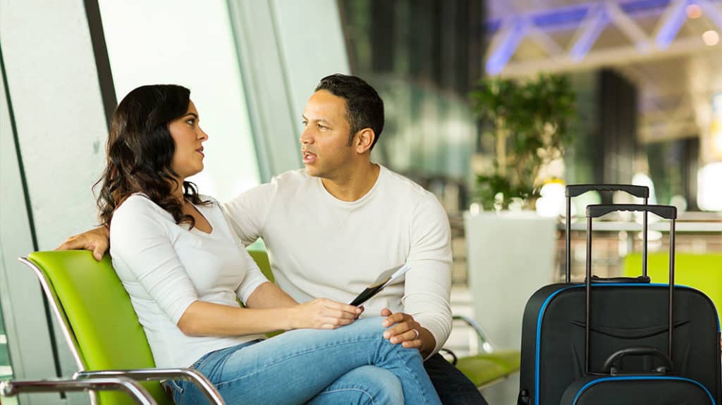 Couple sitting in an airport terminal having a serious conversation, their suitcases positioned next to them.