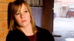 Close up of pensive teen girl leaning against a wall in a city alley