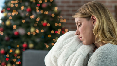 Profile of sad woman sitting, leaning her head against a soft white blanket with a Christmas tree in the background