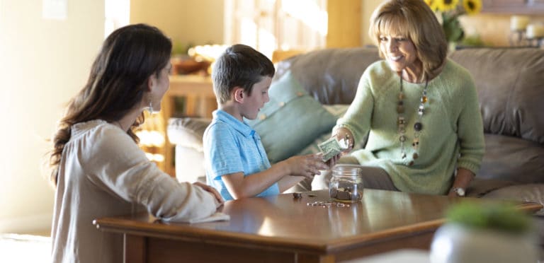 Grandmother hands young grandson money while mother watches, smiling