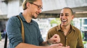 Two men standing outside. One is laughing as the other describes something funny.