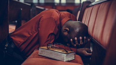 Man praying face down on pew seat with Bible nearby