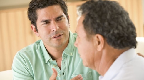 Two men sitting down, the younger one expressing disagreement to the older man