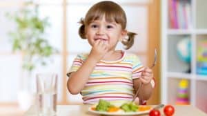 Close up of smiling young girl sitting at a table eating a plate of vegetables