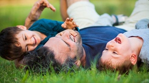 Dad and his two young sons laughing while lying on grass