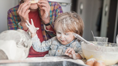 Young, smiling boy covered in baking flour as he and his dad have fun making a mess while preparing something to bake