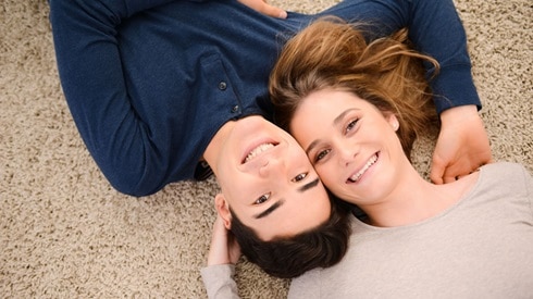 Young, happy couple lying on the floor looking up at the camera; they're lying head to head in opposite directions