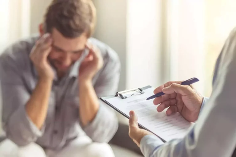 A distressed man holds his head while speaking to a professional holding a clipboard, symbolizing the search for pornography addiction resources.