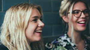 Close up of two young smiling blonde women looking at something to their left off camera