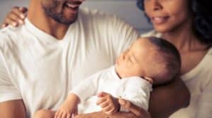 Close up of baby held in dad's arms, with mom standing next to him; both are smiling.