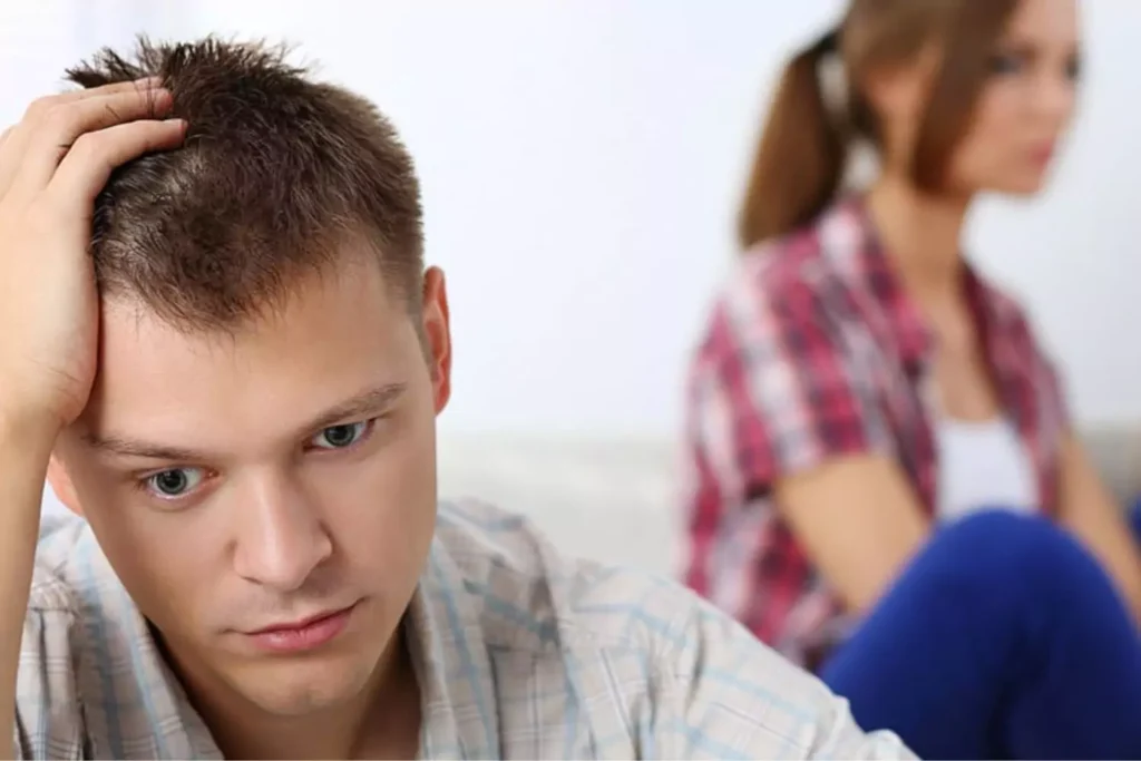 A man appears distressed while sitting beside a woman, symbolizing the emotional impact of relationship challenges such as those that could arise from discovering their spouse is on the Ashley Madison list.