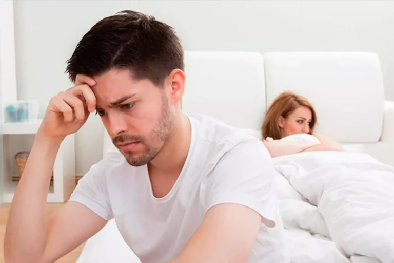 A troubled couple sits apart in a bedroom, both appearing distressed, illustrating the impact of pornography on relationships.