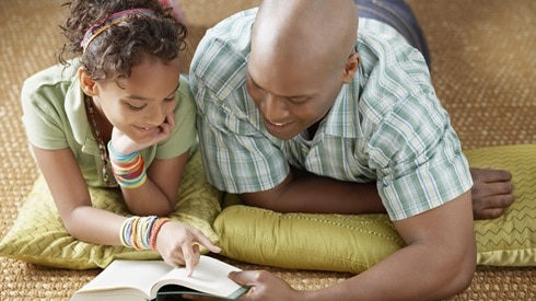 Dad and daughter laying on the floor reading the Bible together and smiling.