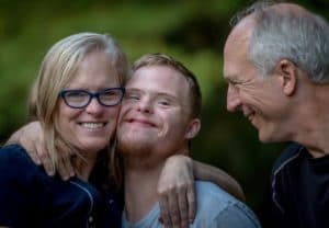 Close up of smiling middle-age couple with mom having a side hug with their grown, special needs son
