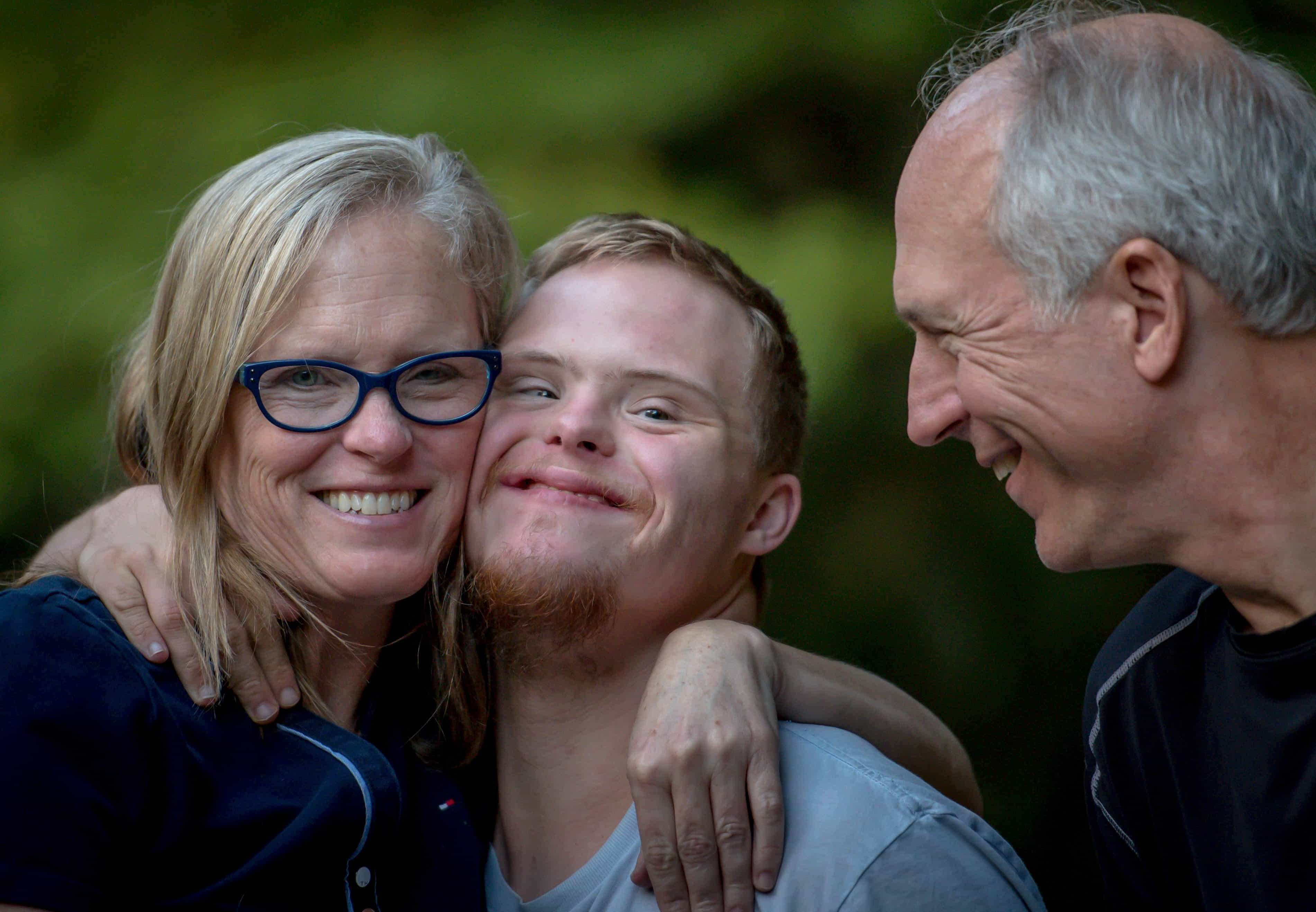 Close up of smiling middle-age couple with mom having a side hug with their grown, special needs son