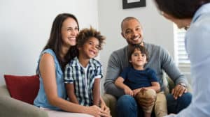 Happy interracial couple sitting on a couch with their two adopted kids talking to a counselor