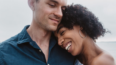 Close up of young interracial couple. She's smiling and leaning her head on his shoulder.