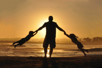 Silhouette of a dad spinning his two kids around on a lakeshore at sunset