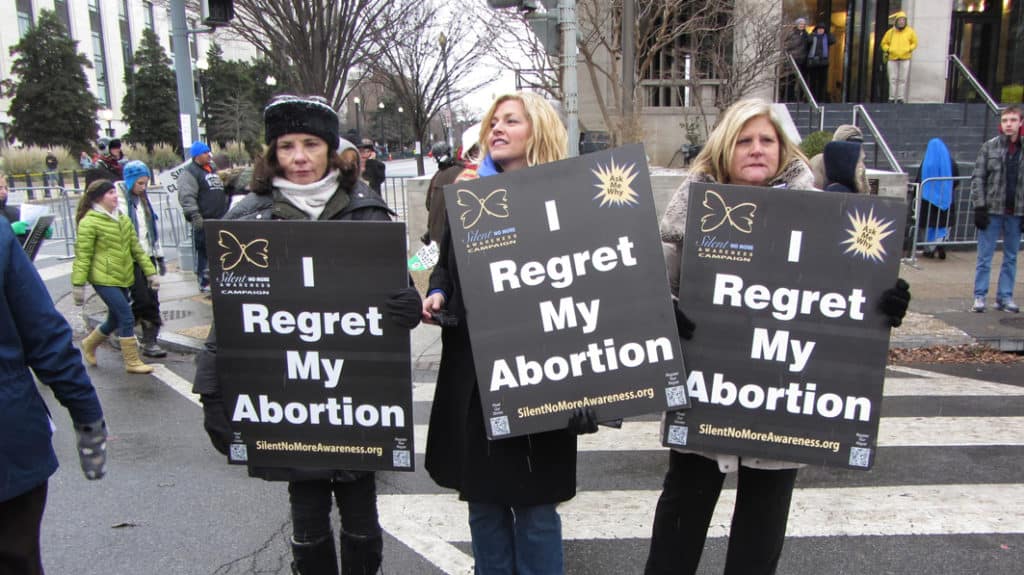 Three women at a pro-life rally near the Supreme Court holding signs that say they regret their abortion