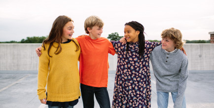 Four pre-teens or young teens standing in a line hanging out, smiling together