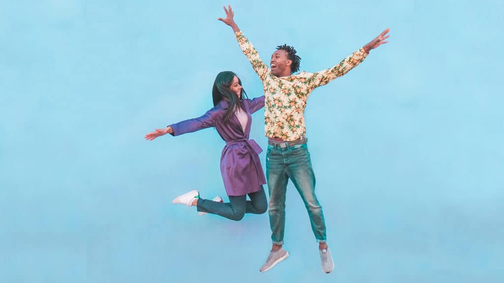 Happy black couple jumping in the air against a light-blue, plain background