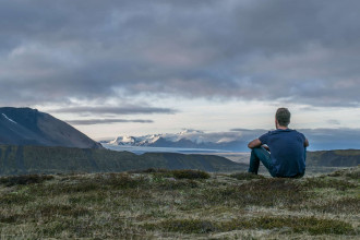 a solitary man sitting with his back to us, looking out at far mountains