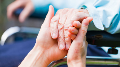 two young hands hold the older hand of someone in a wheelchair
