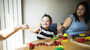 Mother and one of the children with special needs playing together at a table, son giving a fist bump to someone off camera