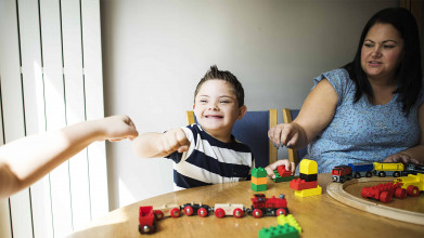 Mother and one of the children with special needs playing together at a table, son giving a fist bump to someone off camera
