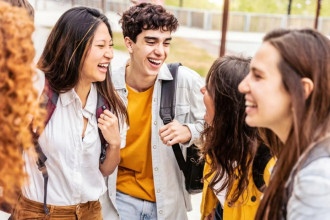 Four pre-teens or young teens standing in a line hanging out, smiling together