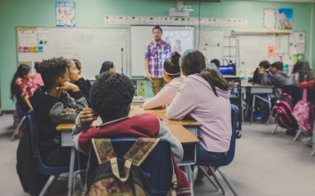 Scene of middle-school children sitting in a classroom listening to their teacher