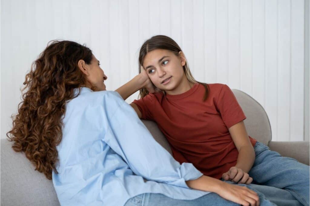 A mom and teen sitting on the couch talking together